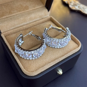 Detailed close-up of C-shaped silver earrings with sparkling cubic zirconia in a jewelry box