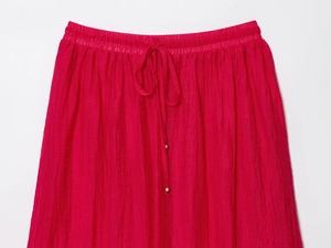 Détail d'une jupe midi plissée rouge avec taille élastique et cordon à perles dorées