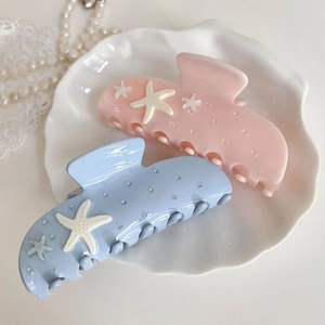 Pinces à cheveux étoile de mer rose et bleue avec strass sur un plateau coquillage
