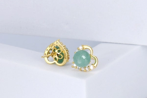 Close-up of heart-shaped gold studs with green round stones and white zircon accents