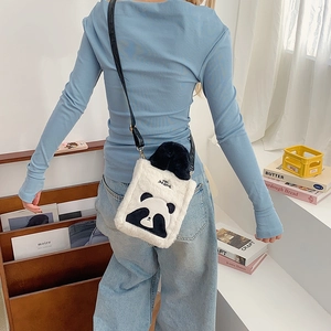 Cute panda-shaped plush crossbody bag with a black strap worn by a model in a cozy room