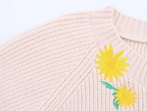 Detail shot of sunflower embroidery and chunky knit texture on beige round neck sweater