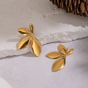Artistic golden leaf-shaped metal stud earrings displayed on natural stone and pinecone