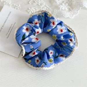 Detail of blue floral scrunchie with white lace trim and yellow flower print on wood