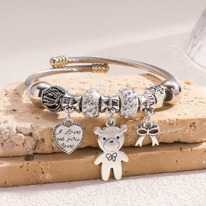 Silver twisted bangle with teddy bear and heart charm on a beige stone base
