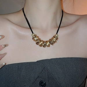 Detail view of a gold twisted ring pendant on a black cord necklace on a model's neck