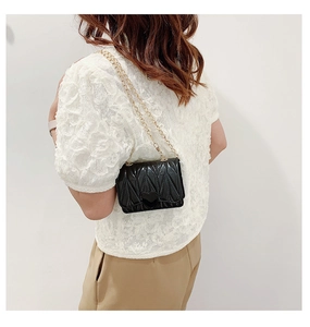 Detail of black quilted crossbody bag with 3D leaf texture and gold chain strap