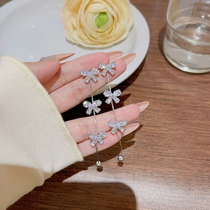 Macro shot of silver bow tassel earrings with sparkling zircons held by hand