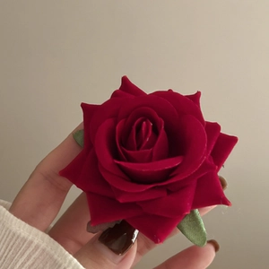 Close-up of red fabric rose hair claw clip with green fabric leaves held in hand