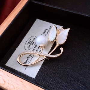 Macro d'une broche tulipe dorée avec pétales en nacre et perle sur une carte vintage