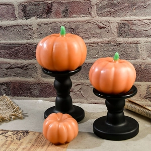 Tre candele a forma di zucca arancione di varie dimensioni su un tavolo autunnale