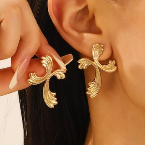 Artistic golden wave relief cross stud earrings worn by a model in a close-up view