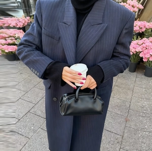 Detail shot of a sleek black matte leather handbag paired with a striped coat in a street setting
