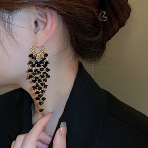 Close-up of black crystal tassel earrings with gold heart charms worn by a model