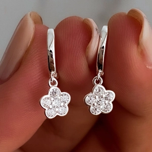 Macro shot of silver flower earrings with sparkling zirconia petals held by hand