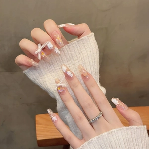 Vue détaillée des faux ongles coffin avec nœuds 3D blancs et motifs floraux