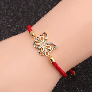 Macro detail of gold-plated butterfly charm with colorful zircons on red woven rope
