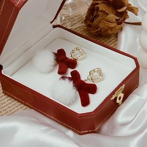 Detail view of red velvet bow earrings with white pom poms in a gift jewelry box