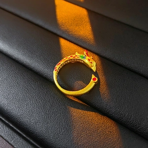 Macro shot of gold phoenix ring with red and green enamel on textured black leather