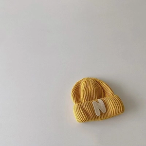 Detailed texture of yellow knitted beanie featuring a white letter N embroidered patch