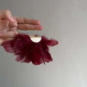 Detail of golden hammered metal earring with burgundy feather fringe held by hand