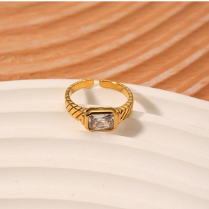 Macro detail of 18k gold ring with square zircon on white wavy ceramic display stand
