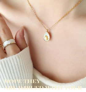 Detail of avocado pendant necklace and gold ring worn on a soft knit sweater