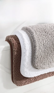 Detail of plush microfiber bath mats in brown, white and grey showing thick soft texture