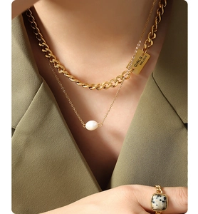 Detail of layered gold cuban chain with engraved tag and freshwater pearl necklace