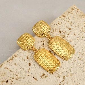 Fashionable gold square earrings with woven waffle texture on a stone pedestal display