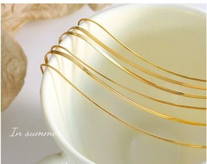 Macro detail of golden double-layer blade chain bracelet draped on a ceramic cup edge