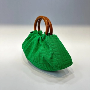 Detail of green pleated handbag with vintage brown wooden handle on textured fabric