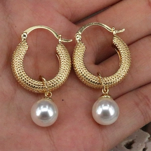 Detail of gold granular hoop earrings with white pearl pendants held in hand