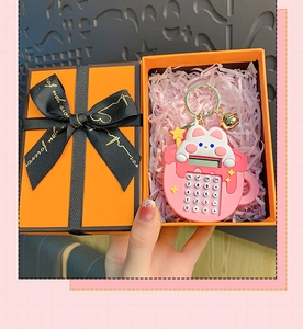 Pink cartoon calculator keychain with golden clasp and bell inside an orange gift box