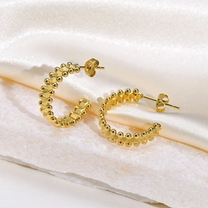 Golden C-hoop twisted earrings with beaded texture on white marble and silk background