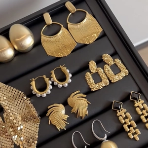 Collection of golden geometric heart and pearl earrings in a black jewelry display tray
