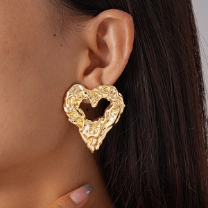 Close-up of a model wearing a gold hollow heart earring with unique hammered metal texture