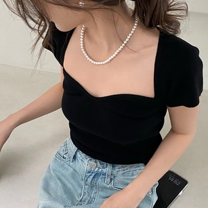 Detailed close-up of a vintage pearl necklace styled with a black square neck knit top