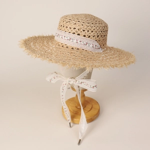 Detail of raffia straw hat with white floral lace ribbon and frayed edge brim