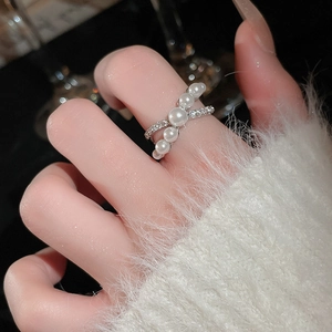 Detailed view of crossover ring with white pearls and sparkling rows of zircon on finger