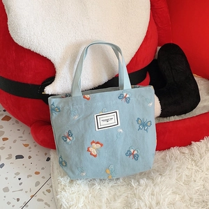 Détail du sac en toile bleu clair avec broderies papillons colorées et logo