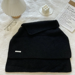 Detail of black ribbed knit scarf with golden buttons and branding label on fabric