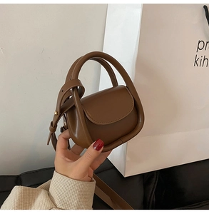 Mini sac bandoulière en cuir marron tenu à la main avec une poignée ronde tendance