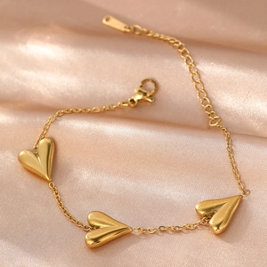 Detail of gold-plated stainless steel bracelet with three heart charms on pink silk fabric