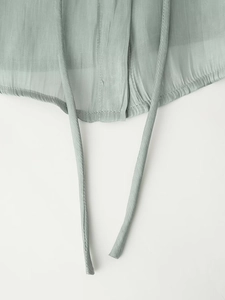 Detailed close-up of light sage green chiffon blouse hem with delicate tie strings