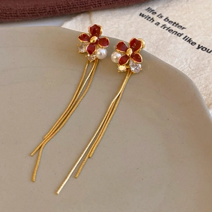Detail shot of deep red flower earrings with golden tassels and delicate pearl accents