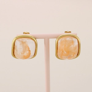 Gros plan de boucles d'oreilles carrées dorées avec résine orange sur support rose
