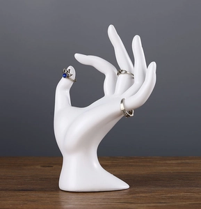White hand-shaped resin jewelry display stand for rings and bracelets on walnut wood surface