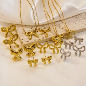 Elegante goldene und silberne Schleifenketten und Ohrringe auf Seide und beigem Steinbelag