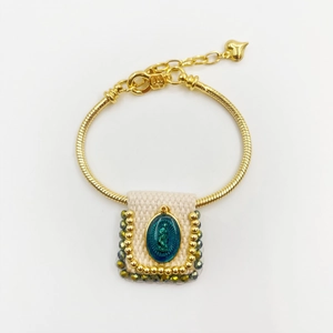 Detailed view of religious Virgin Mary pendant on golden beaded bracelet with blue enamel
